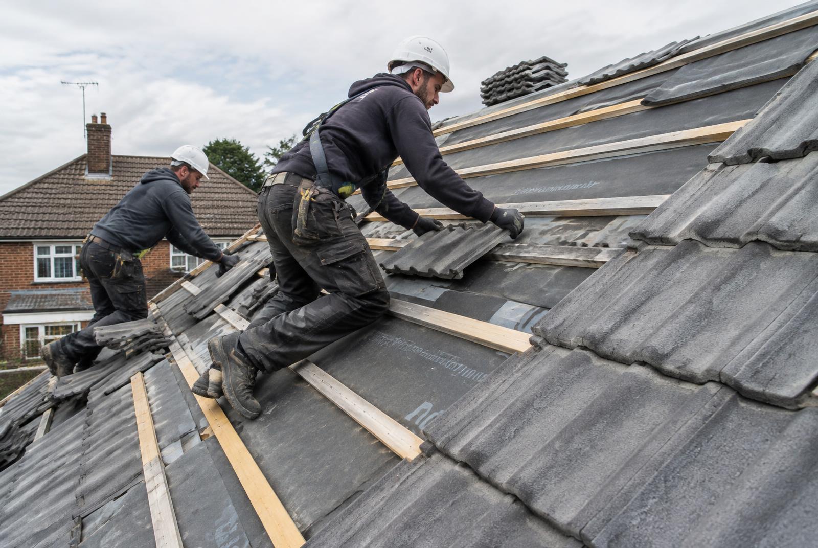 Two roofers installing new concrete tiles on a pitched roof